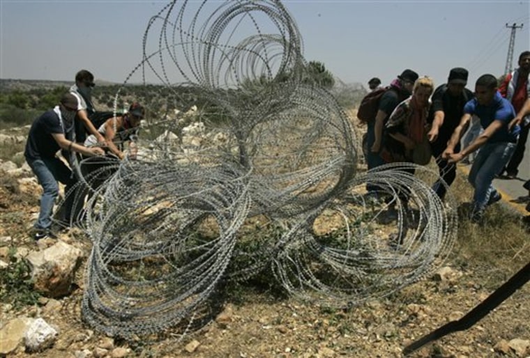 Palestinians and foreign activists damage a part of the Israeli security barrier near the West Bank town of Qalqiliya, on Monday, July 11. Witnesses say foreign activists have joined Palestinians in tearing down part of an Israeli fence in the West Bank Monday. They said some of the foreigners arrived in past few days, part of an effort to fly in protesters to demonstrate in the West Bank. 